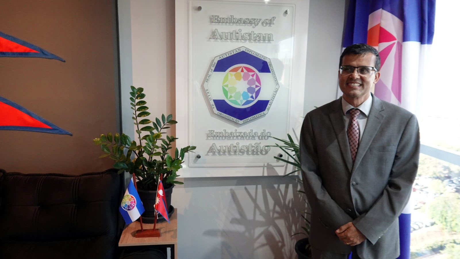 Perto da placa da Embaixada do Autistão, com os símbolos do Nepal e do Autistão.